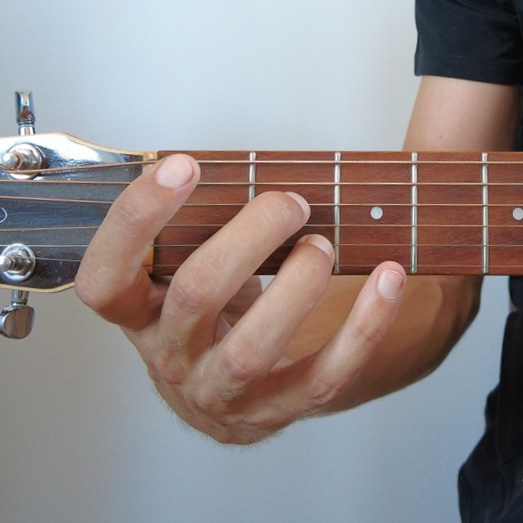 Photo d'une main faisant un accord de La7 à la guitare