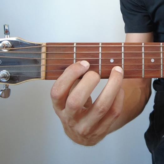 Photo d'une main faisant un accord de Ré à la guitare