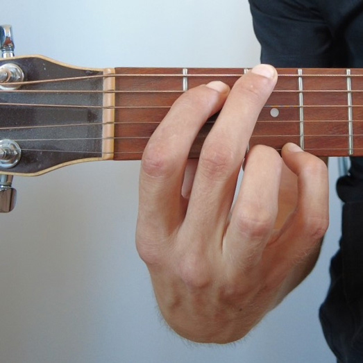 Photo d'une main faisant un accord de Sol à la guitare